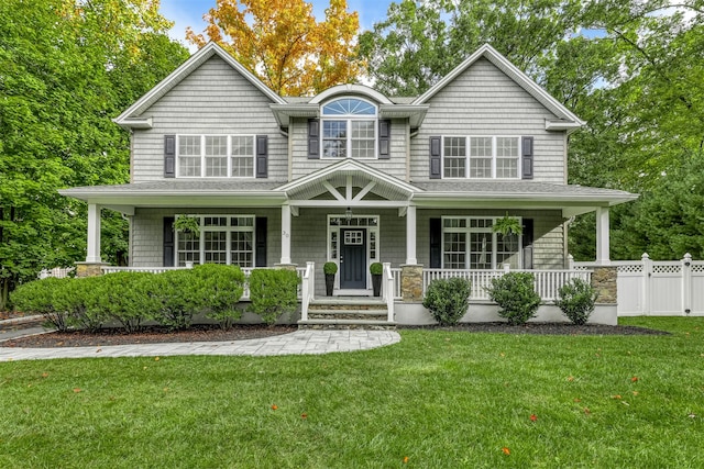 view of front facade featuring covered porch, a front yard, and fence