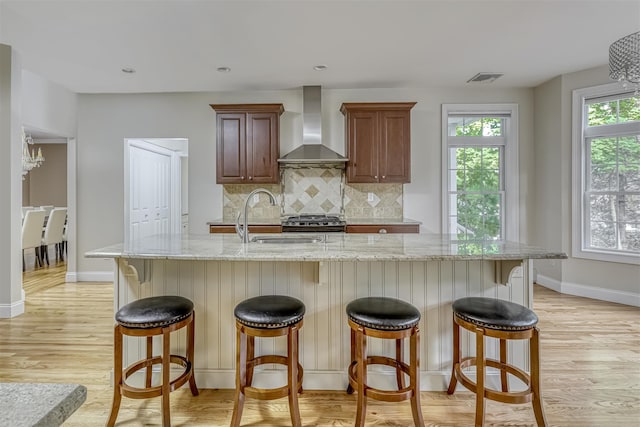 kitchen featuring light wood-type flooring, wall chimney range hood, backsplash, visible vents, and a sink