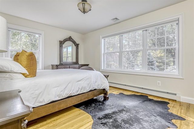 bedroom with visible vents, a baseboard radiator, multiple windows, and wood finished floors