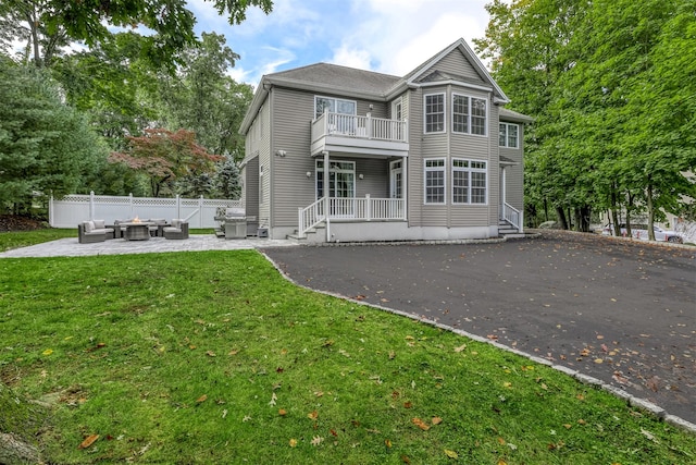back of house featuring an outdoor living space, a lawn, a patio, fence, and a balcony