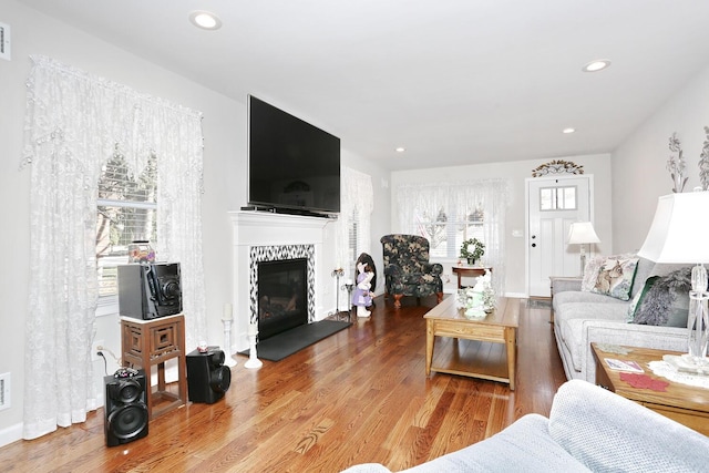 living area with a tiled fireplace, visible vents, recessed lighting, and wood finished floors