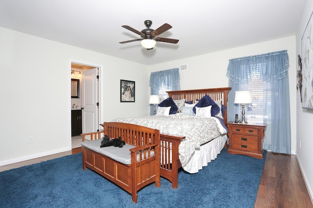 bedroom with visible vents, baseboards, a ceiling fan, ensuite bath, and wood finished floors