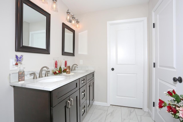 full bath featuring marble finish floor, double vanity, baseboards, and a sink