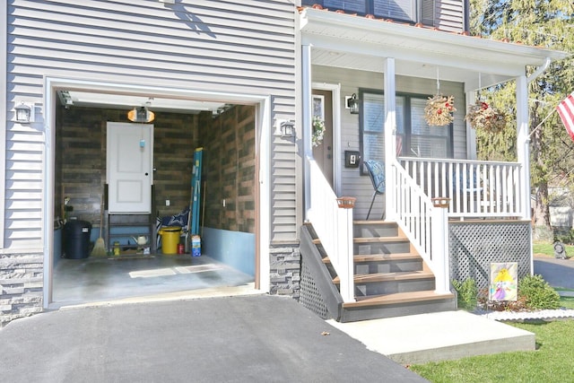 doorway to property featuring a porch, driveway, a garage, and stone siding