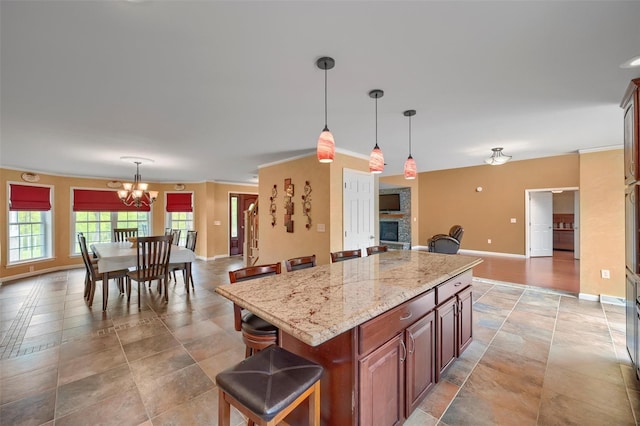 kitchen with hanging light fixtures, baseboards, a chandelier, a kitchen island, and light stone counters