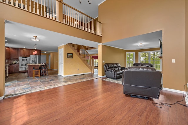 living area with baseboards, stairway, a towering ceiling, and wood finished floors