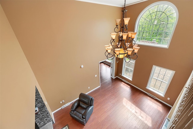 foyer featuring a towering ceiling, baseboards, an inviting chandelier, crown molding, and wood finished floors