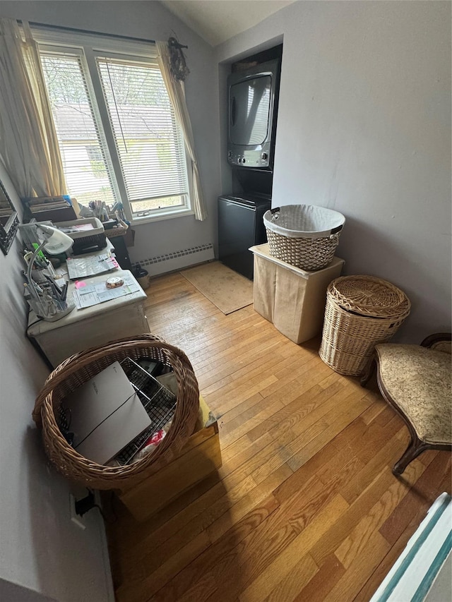 interior space featuring a baseboard radiator, light wood-style floors, lofted ceiling, and stacked washer and dryer