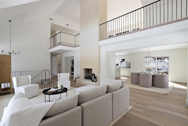 living room featuring a chandelier, a high ceiling, stairs, visible vents, and wood finished floors