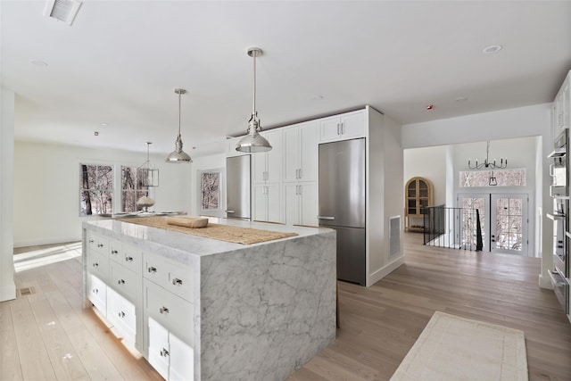 kitchen featuring visible vents, light wood-type flooring, stainless steel refrigerator, and light stone countertops