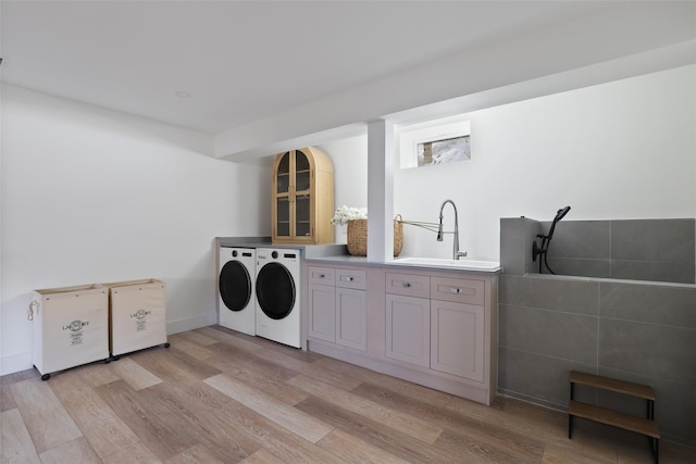 clothes washing area with light wood finished floors, independent washer and dryer, a sink, and cabinet space