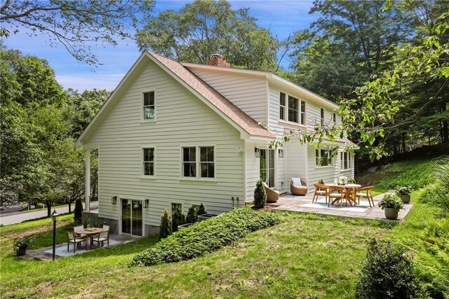 rear view of property with a patio, a yard, and roof with shingles