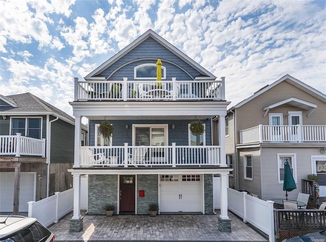 view of front of property with an attached garage, stone siding, a balcony, and fence