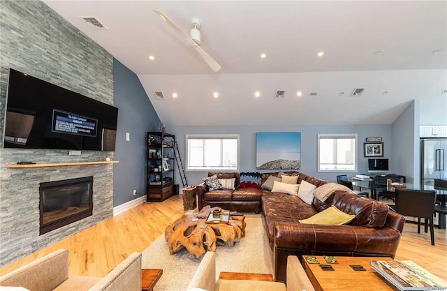 living room featuring a stone fireplace, a healthy amount of sunlight, and wood finished floors