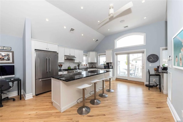 kitchen with white cabinets, stainless steel appliances, a center island, a kitchen bar, and under cabinet range hood