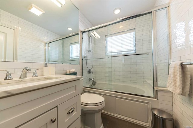 full bathroom featuring combined bath / shower with glass door, vanity, tile walls, toilet, and tile patterned flooring