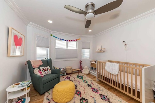 bedroom featuring recessed lighting, wood finished floors, ornamental molding, a nursery area, and ceiling fan