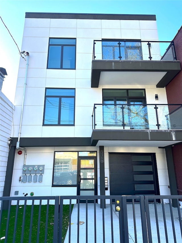 view of front of home with an attached garage, stucco siding, a balcony, and a fenced front yard