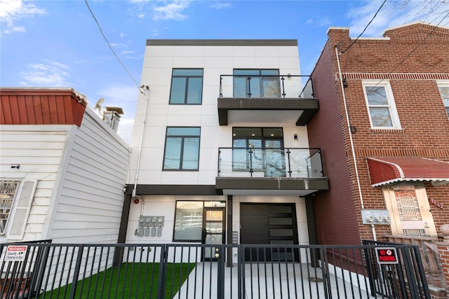 contemporary home featuring an attached garage, a fenced front yard, stucco siding, and a balcony