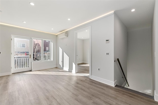 unfurnished living room with light wood finished floors, a wall mounted air conditioner, baseboards, and recessed lighting