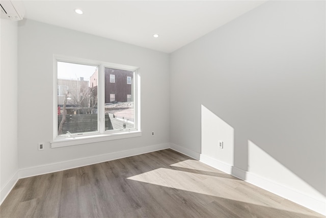 spare room with baseboards, recessed lighting, wood finished floors, and a wall mounted air conditioner