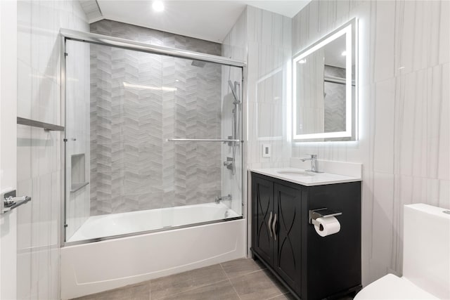 bathroom featuring combined bath / shower with glass door, vanity, tile walls, and toilet