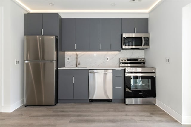 kitchen with stainless steel appliances, gray cabinetry, baseboards, and a sink