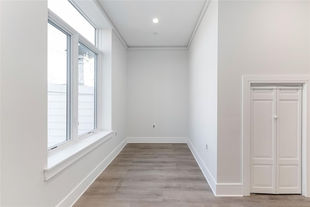 empty room with crown molding, baseboards, and light wood-style floors
