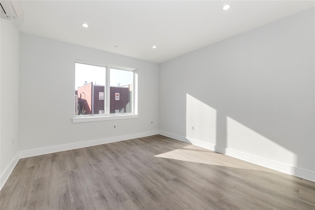 unfurnished room featuring recessed lighting, baseboards, a wall unit AC, and wood finished floors