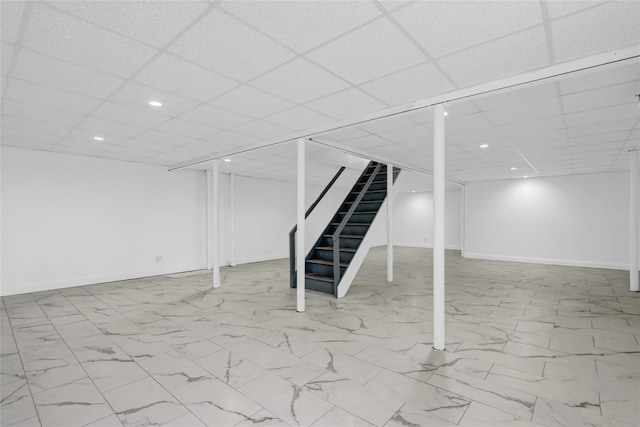 finished below grade area with a drop ceiling, recessed lighting, marble finish floor, stairs, and baseboards