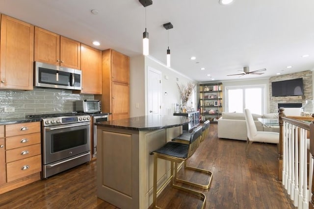 kitchen with a center island, a stone fireplace, a ceiling fan, stainless steel appliances, and dark wood-type flooring