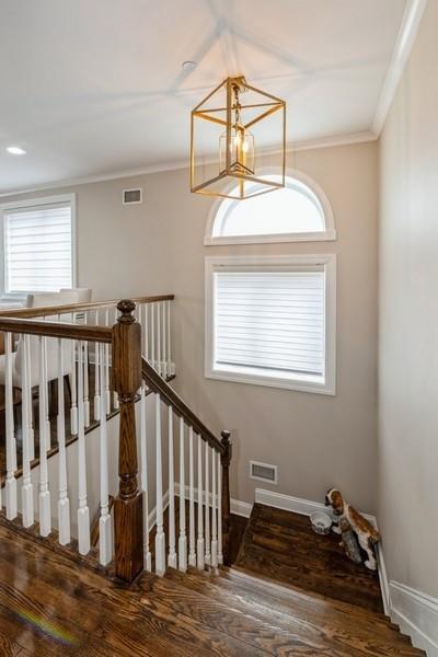 stairway with crown molding, wood finished floors, baseboards, and visible vents