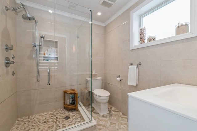 bathroom with visible vents, toilet, tile walls, crown molding, and a shower stall