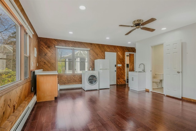clothes washing area with washer / clothes dryer, wooden walls, ceiling fan, a baseboard radiator, and a sink