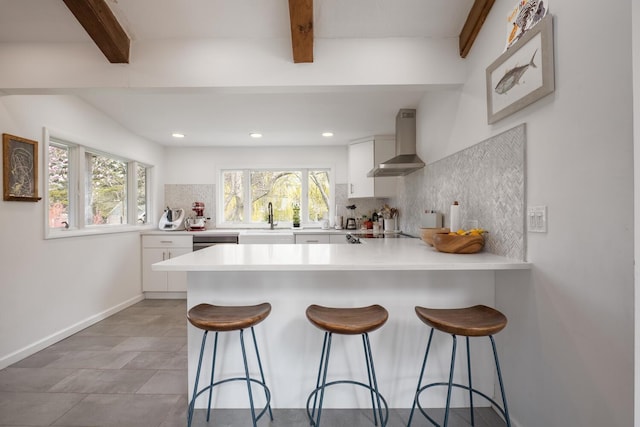 35 Turtle Cove Ln, Huntington, NY 11743 - kitchen featuring wall chimney exhaust hood, beamed ceiling, a peninsula, white cabinets, and tasteful backsplash