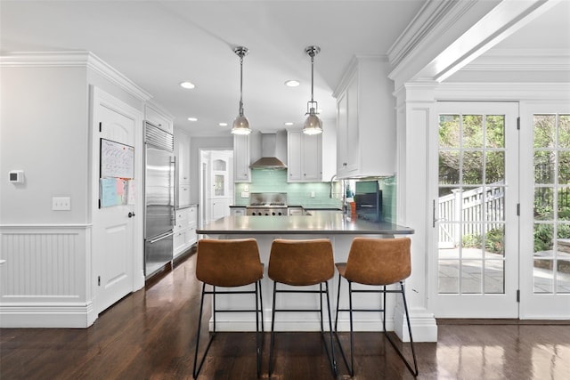 kitchen featuring built in fridge, wall chimney range hood, range, dark wood-type flooring, and crown molding
