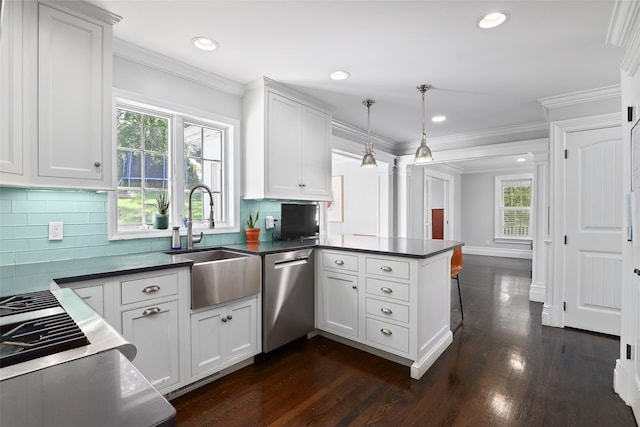 kitchen featuring stainless steel dishwasher, a sink, dark countertops, a peninsula, and dark wood-type flooring