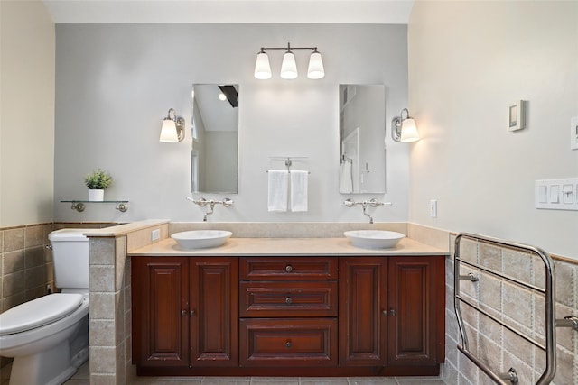 bathroom with tile walls, toilet, wainscoting, and double vanity