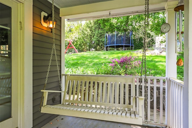 wooden terrace featuring a porch, a trampoline, and a yard