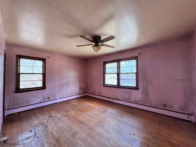 empty room with wood-type flooring, a ceiling fan, and a baseboard heating unit