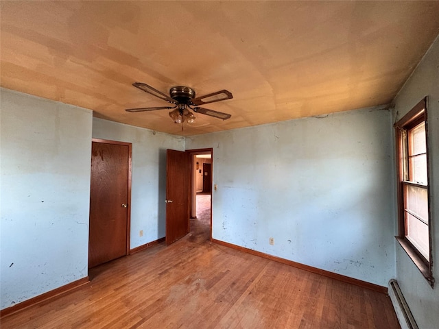 unfurnished bedroom with a baseboard radiator, wood finished floors, a ceiling fan, and baseboards