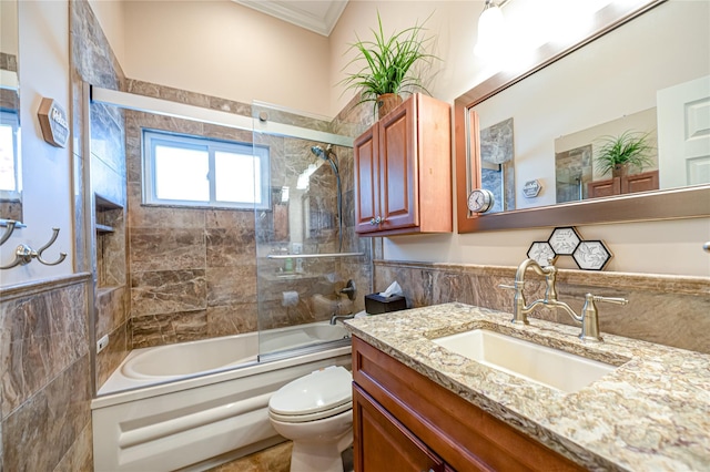 bathroom featuring toilet, combined bath / shower with glass door, crown molding, tile walls, and vanity