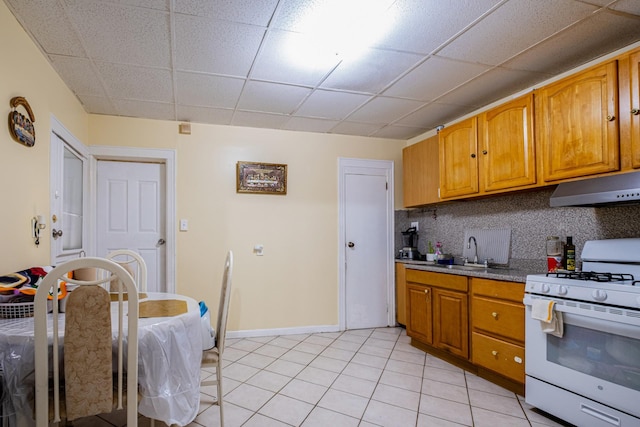101-14 95th St, Ozone Park, NY 11416 - kitchen with white gas range, under cabinet range hood, a sink, a paneled ceiling, and brown cabinetry