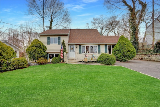 split level home featuring roof with shingles, a front lawn, aphalt driveway, and a porch