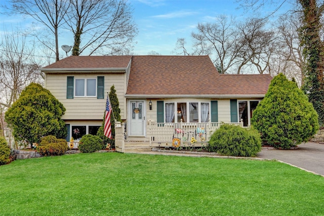 tri-level home with a front yard, covered porch, and roof with shingles