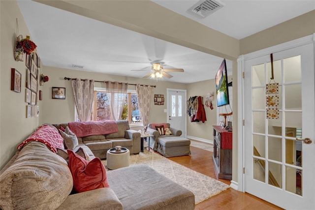 living room featuring light wood-style floors, visible vents, baseboards, and ceiling fan