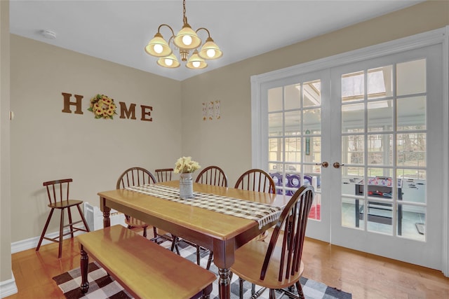 dining area with french doors, light wood-style flooring, an inviting chandelier, and baseboards