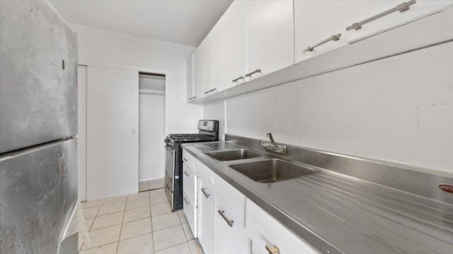 kitchen featuring light tile patterned floors, white cabinets, a sink, dark countertops, and stainless steel appliances
