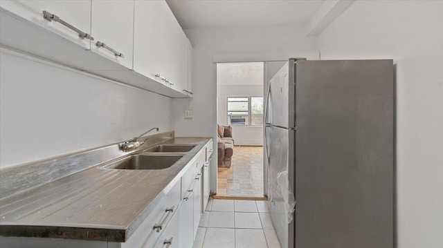 kitchen featuring freestanding refrigerator, a sink, white cabinets, and light tile patterned floors