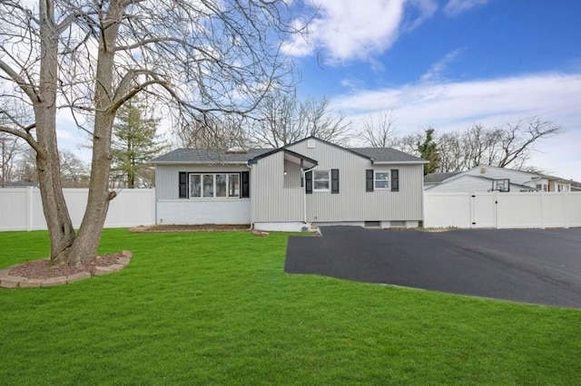 view of front of house featuring roof with shingles, fence, a front lawn, a gate, and driveway